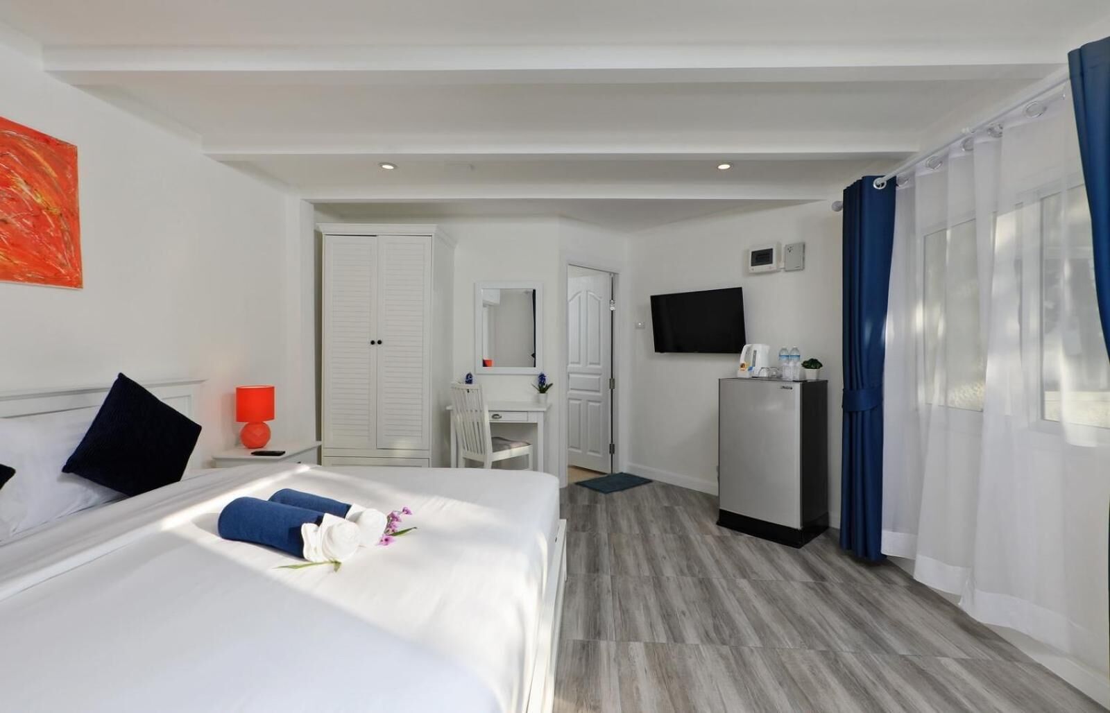 Quarto de hotel com cama, escrivaninha, televisão e frigorífico.