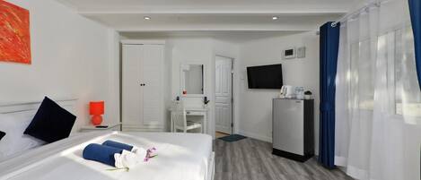 Quarto de hotel com cama, escrivaninha, televisão e frigorífico.