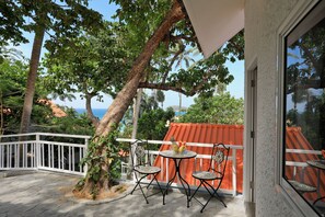A balcony with a white railing, two chairs, a small round table, and a fruit bowl. - Kata White Villas (Karon)