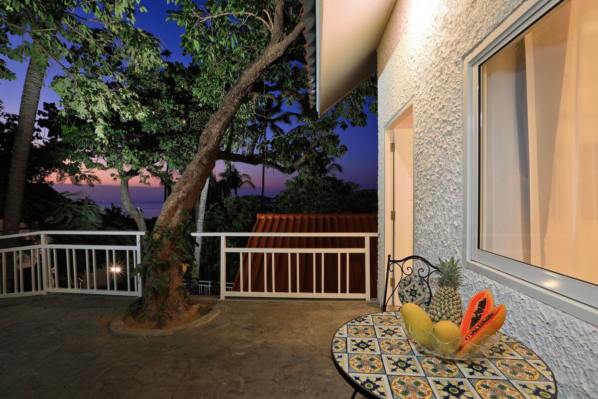 A patio with a tiled table, a fruit bowl, and a view of a sunset.