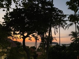 A sunset view with palm trees and a building in the foreground.