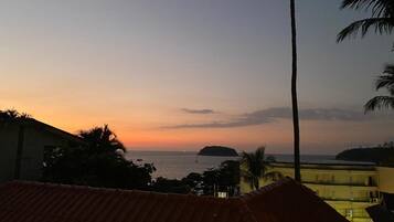 A sunset view from a balcony with a tiled roof, overlooking a calm sea and distant islands.