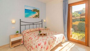 Een slaapkamer met een bed, een nachtkastje, een schilderij van een strand en een schuifdeur naar een balkon.