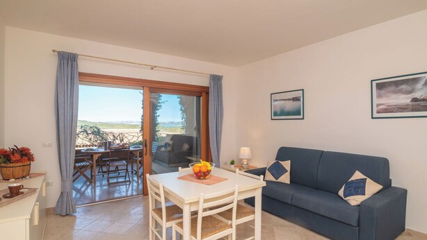 A room with a dining table, a blue sofa, and a view through a sliding glass door. - Cosy apartment for 4 guests with pool, A/C, WIFI, terrace and pets allowed (Santa Teresa Gallura)