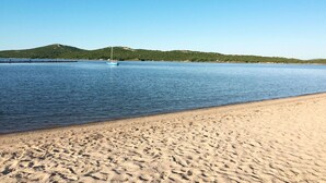 Una playa con un bote en aguas tranquilas, orilla de arena y colinas verdes al fondo.