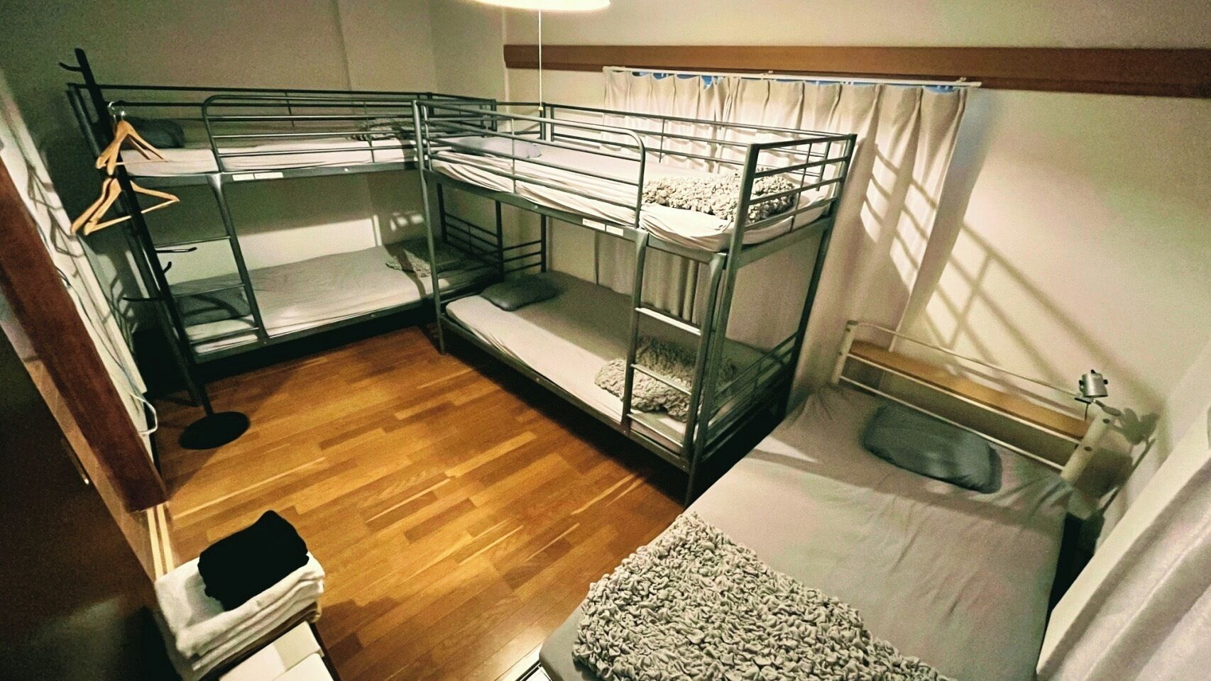 A bunk bed room with a wooden floor, a small table, and a curtain.