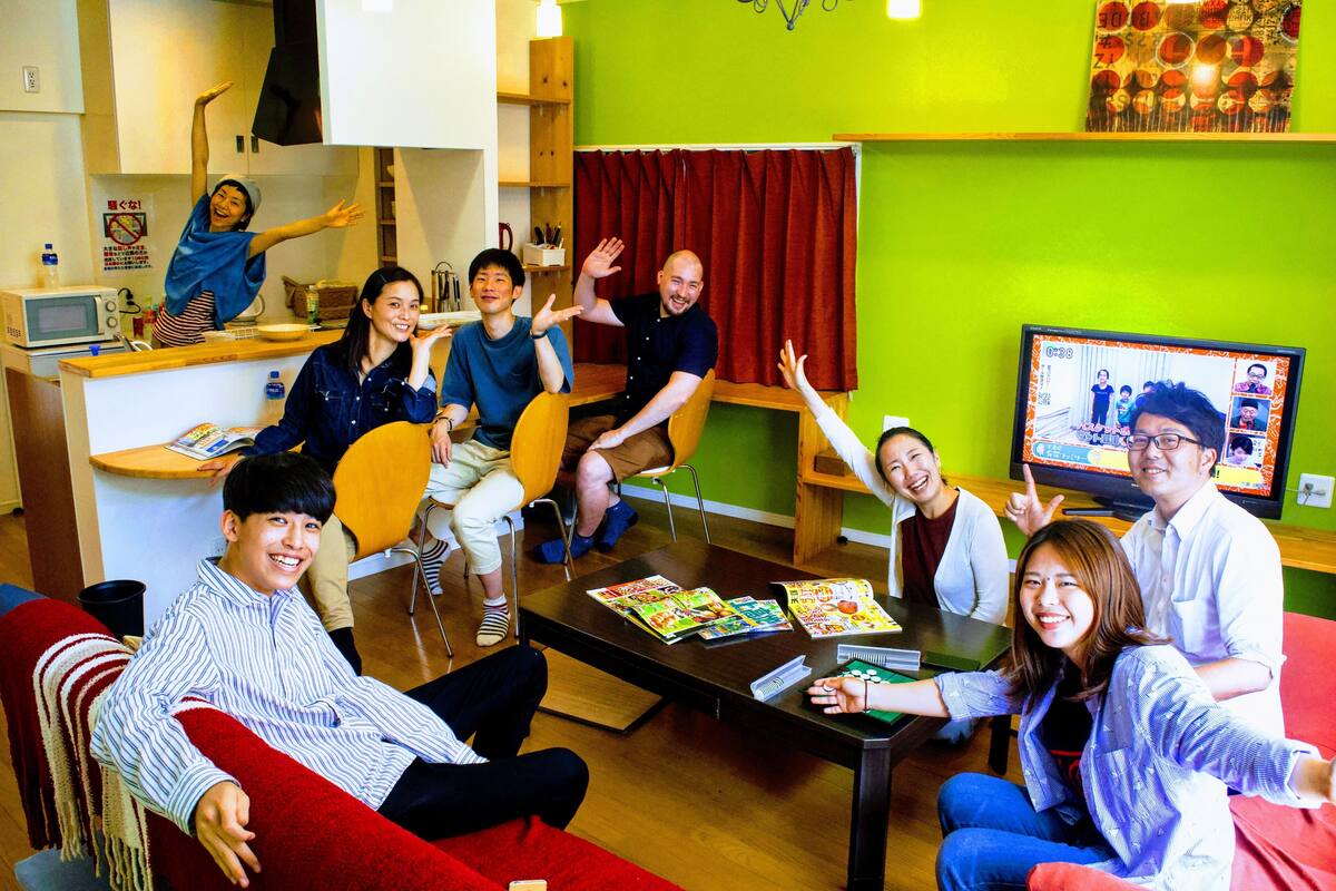 A group of people in a room with a television, a table with magazines, and a red couch.