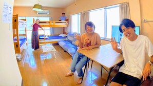 A room with bunk beds, a sofa, a table, and a hanging light fixture. - Guesthouse LuLuLu Atago (Kochi)