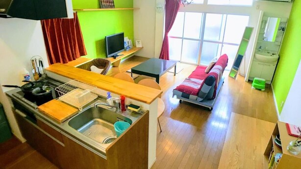 A compact living space with a kitchenette, a dining area, and a small seating area with a sofa and a chair. - Guesthouse LuLuLu Atago (Kochi)