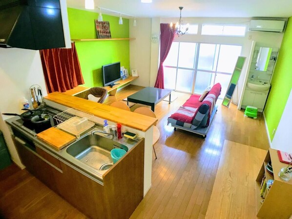 Un espacio habitable compacto con kitchenette, comedor y una pequeña zona de estar con sofá y sillón.