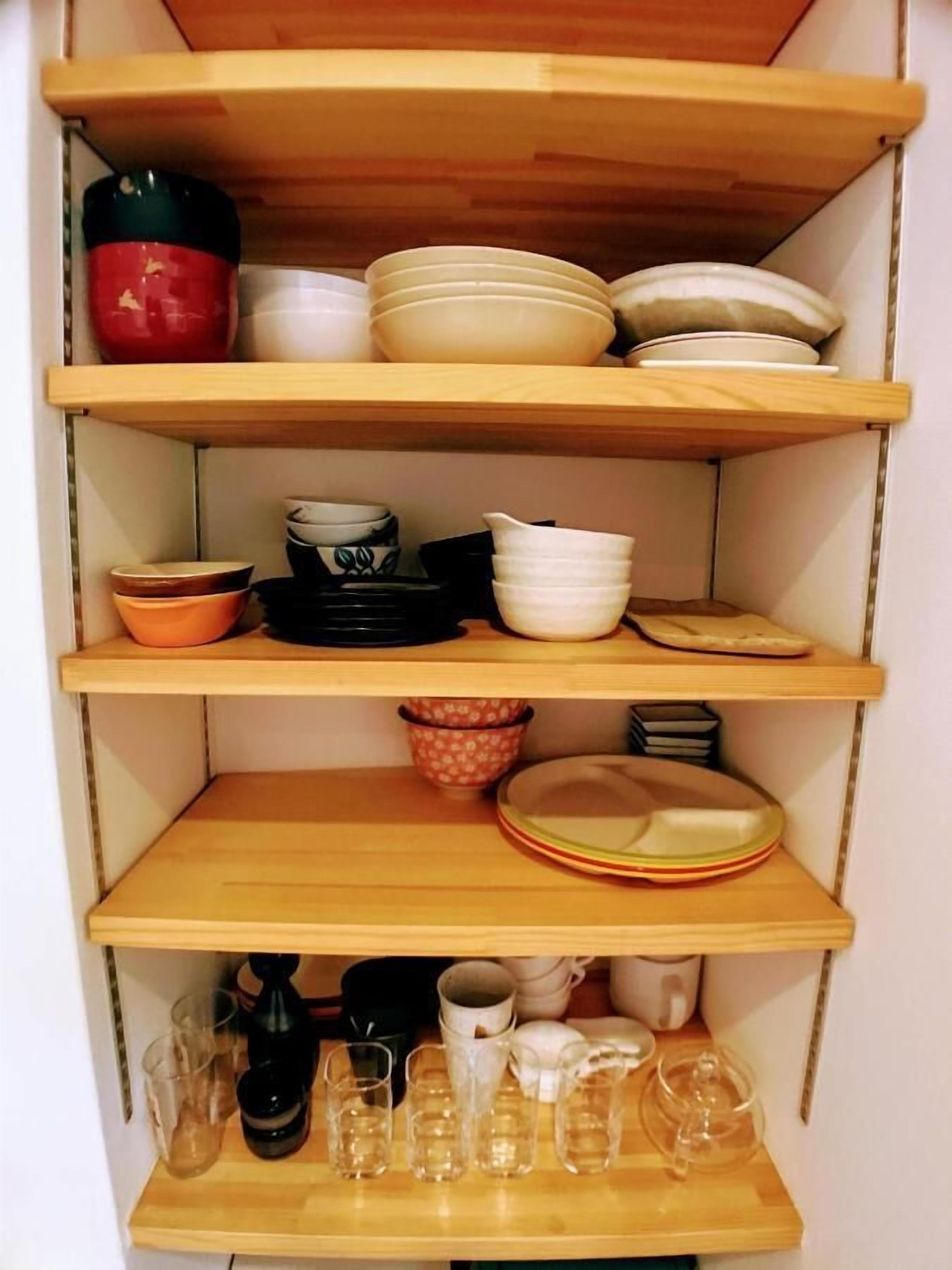 Een keuken met houten planken waarop verschillende serviesdelen en drinkglazen staan.