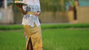 Eine Person steht in einem grasbewachsen Feld, im Hintergrund ist ein Gebäude zu sehen.