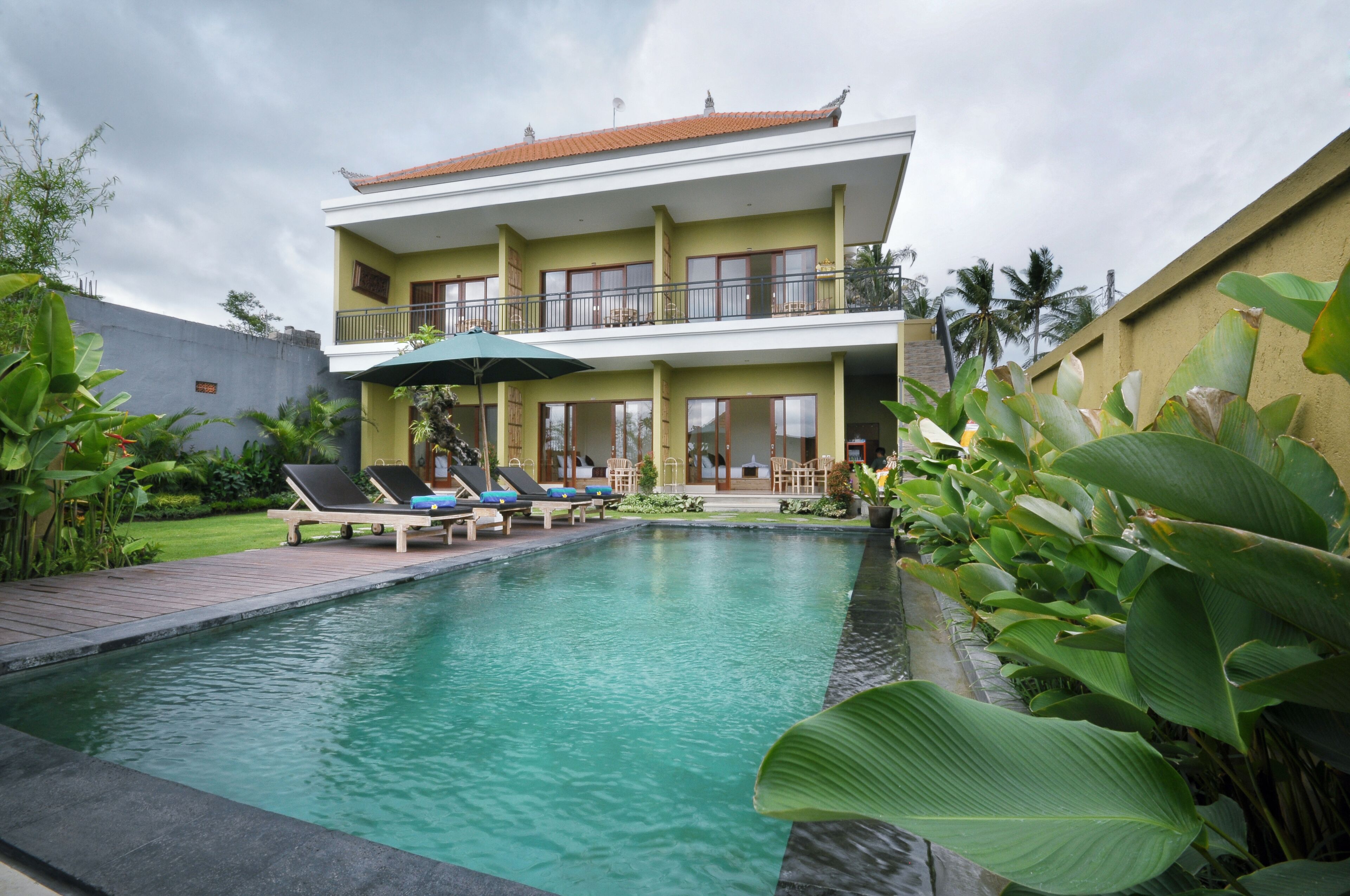 Un bâtiment à deux étages doté d’une piscine, de chaises longues et de plantes tropicales.