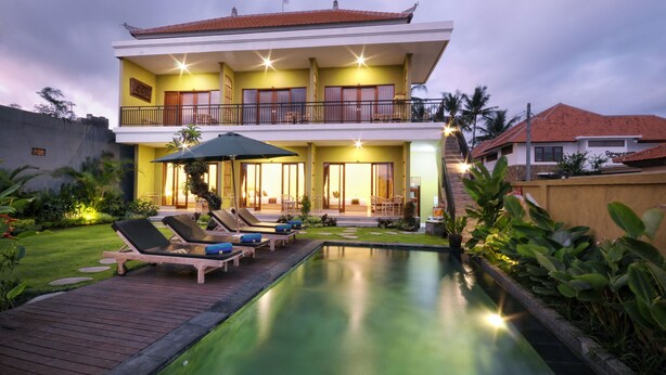 Ein zweistöckiges Haus mit Swimmingpool, Liegestühlen und einem gepflegten Garten.