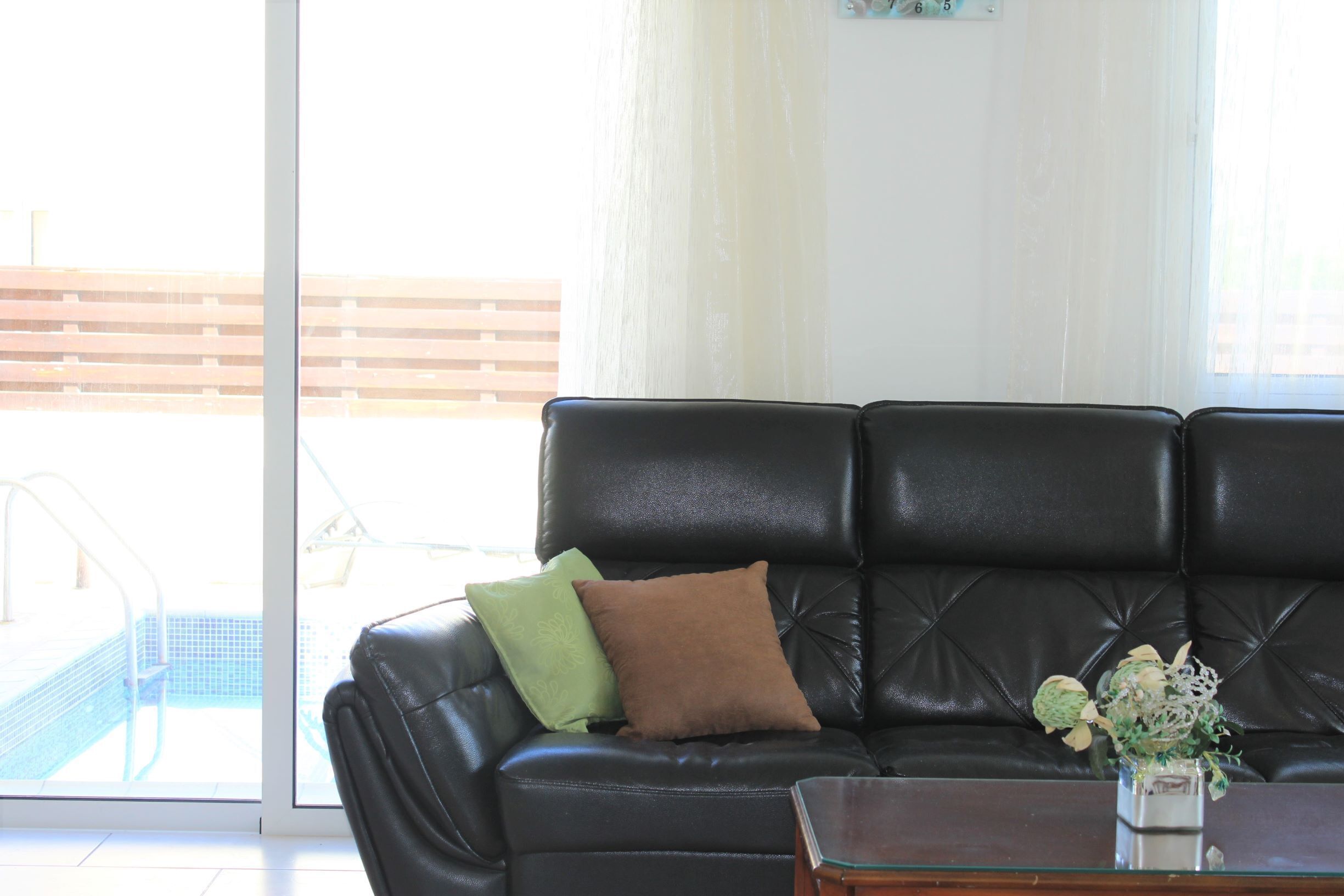 Ein schwarzes Ledersofa mit zwei Kissen, einem Glastisch und einer Vase mit Blumen.