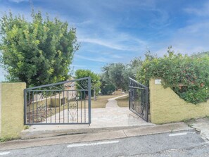 Enter a serene oasis through the beautifully designed metal gate, flanked by lush greenery and a paved pathway.