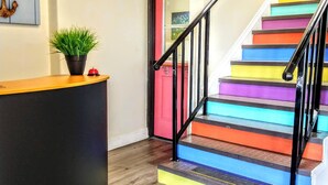 Eine Treppe mit bunten Stufen führt zu einem Raum mit Holzboden und einer Rezeption mit einer Pflanze.