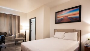 Ein Hotelzimmer mit einem großen Bett, einem Schreibtisch mit Stuhl, einer Lampe und einem Bild an der Wand.