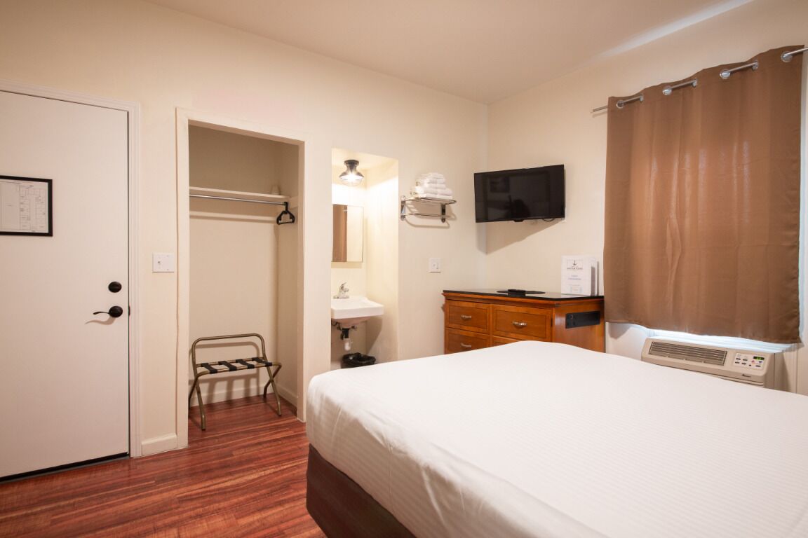 A hotel room with a bed, a TV mounted on the wall, a bathroom with a shower curtain, and a wooden dresser.