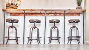 Eine Bar mit einer Holztresen, vier Barhocker, einer Pendelleuchte und zwei Topfpflanzen.
