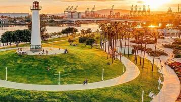 A park with a central monument, pathways, and a waterfront with industrial structures in the background.