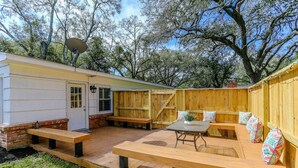 Un jardin avec une terrasse en bois, un barbecue, une table avec des chaises et une clôture en bois.