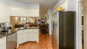 Une cuisine moderne avec des meubles blancs, un réfrigérateur en acier inoxydable et un coin repas comprenant des chaises et une table en bois.