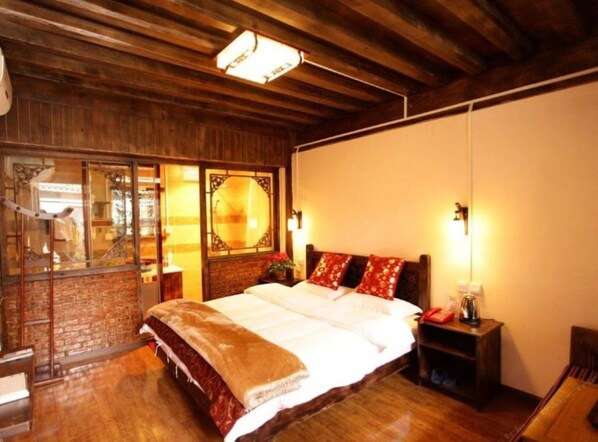 Un dormitorio acogedor con techo de madera, una cama grande con ropa de cama roja y blanca, una mesita de noche y una ventana con vistas al exterior.