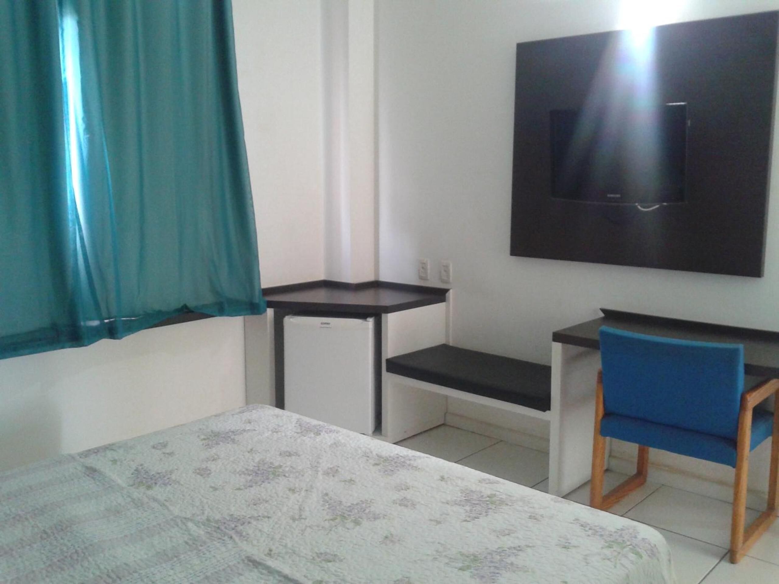 Una habitación pequeña con cama, escritorio, silla y televisor montado en la pared.