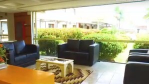 A living area with a sofa, armchairs, a coffee table, and a view of a garden through a glass door. - Itacaiunas Hotel (Maraba)