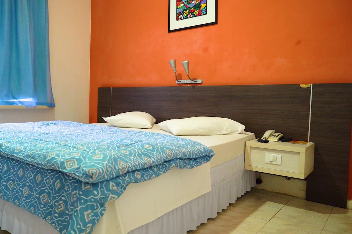A bedroom with a bed, a nightstand, a telephone, and a picture on the wall.