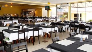 A restaurant with multiple tables and chairs, a kitchen area, and large windows. - Itacaiunas Hotel (Maraba)