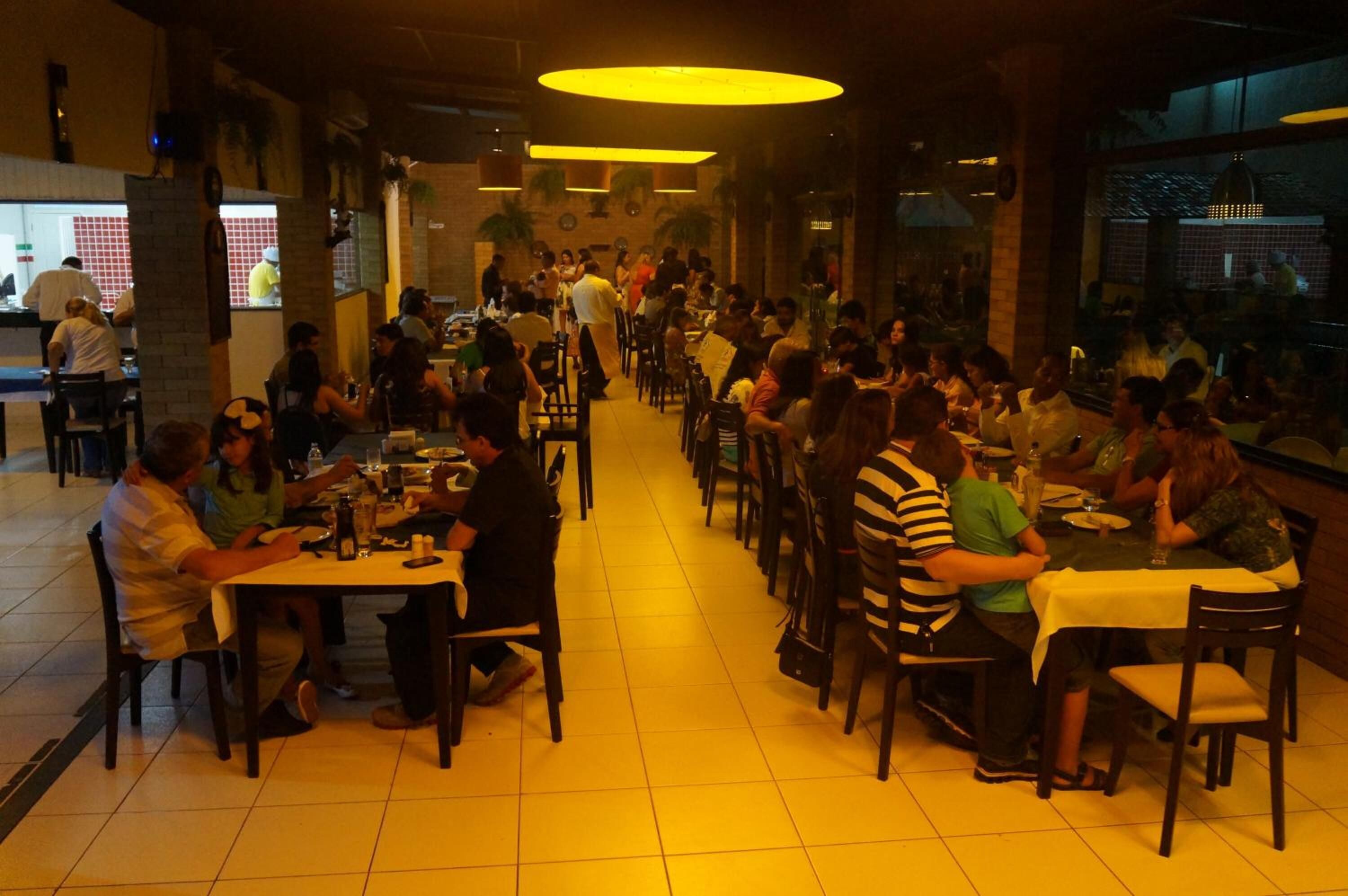 A busy restaurant with multiple dining tables and chairs, a tiled floor, and a warm interior lighting.