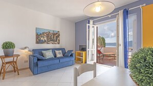 Una sala de estar moderna con un sofá azul, una mesa de comedor y un balcón con vista al mar.