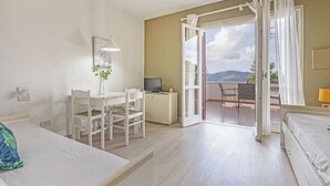 Una habitación con cama, escritorio, silla, televisor y balcón con vistas.