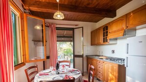 A cozy kitchen with wooden cabinets, a dining table set for two, and a view through an open door to an outdoor area. - Nice apartment in villa for 4 guests with WIFI, TV, terrace and pets allowed (Barabarca)