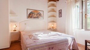 Een slaapkamer met een bed, twee bedlampen, een schilderij aan de muur en een raam met gordijnen.