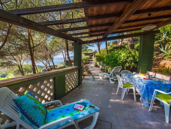 A covered outdoor seating area with chairs and a table, overlooking a scenic view of trees and a body of water.