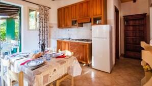 A kitchen with wooden cabinets, a white refrigerator, and a dining table set with plates and glasses. - Nice apartment in villa for 5 people with WIFI, TV, terrace and pets allowed (Barabarca)