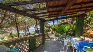 A covered patio with outdoor seating, a view of the sea, and a wooden pergola structure.