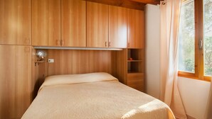 A bedroom with wooden cabinets, a bed with a beige cover, and a window with curtains.