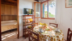 A cozy dining area with a round table set for four, wooden chairs, a television on a stand, and a window with curtains.