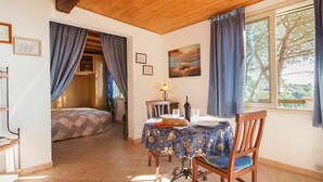 A cozy room with a bed, a dining table with chairs, a window with curtains, and a painting on the wall. - Beautiful apartment in villa for 2 people with WIFI, TV, terrace and pets allowed (Capoliveri)