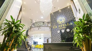 A hotel lobby with a reception desk, a chandelier, and a decorative wall with a clock. - La Stella Hotel (Bai Chay)