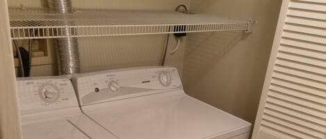 A compact laundry room with a front-loading washer and dryer, a metal vent, and a white door.