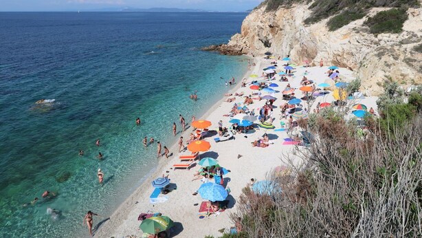 A beach with clear turquoise water, people swimming and sunbathing under colorful umbrellas, and rocky cliffs in the background. - Nice apartment for 4 people with WIFI, TV and terrace (Portoferraio)