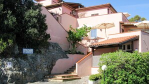 A multi-story building with a stone staircase leading to a door, surrounded by greenery and a clear sky. - Nice apartment for 4 people with WIFI, TV and terrace (Portoferraio)