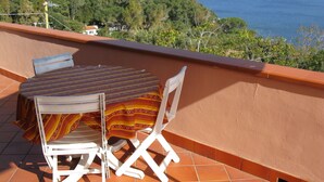 A terrace with a table and two chairs, overlooking a coastal landscape with a view of the sea and a hill with vegetation. - Nice apartment for 4 people with WIFI, TV and terrace (Portoferraio)