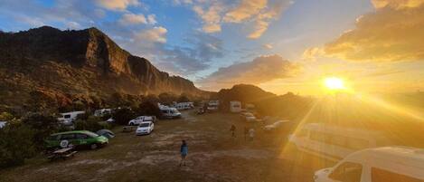 Un camping con vehículos recreativos y automóviles estacionados en un área verde, con montañas al fondo.