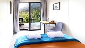 Une chambre d’hôtel comprenant un lit, une chaise, une table et une vue sur la verdure et les montagnes, accessible par une porte coulissante.